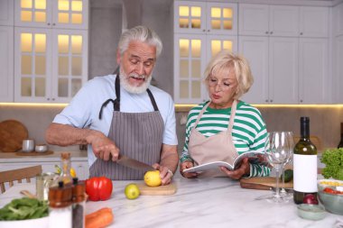 Yaşlı çift mutfaktaki mermer masada birlikte yemek pişiriyor.