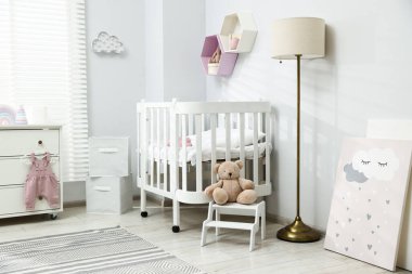 Şık beyaz beşik, çekmeceler, lamba, oyuncaklar ve dekorasyon malzemeleri bebek odasında. İç tasarım