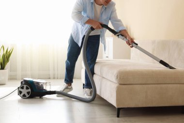 Kanepeyi elektrikli süpürgeyle temizleyen adam, yakın çekim.