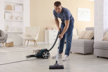 Evin zeminini elektrikli süpürgeyle temizleyen adam.