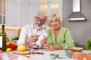 Yaşlı çift mutfakta yemek pişirirken beyaz şarap içiyor.