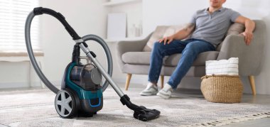 Evdeki kanepede dinlenen adam, elektrik süpürgesine odaklan.