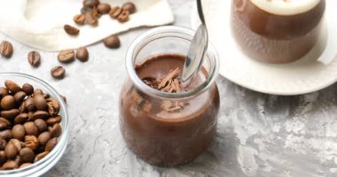 Gri desenli masadaki kavanozdan lezzetli çikolatalı panna cotta alan kadın, yakın plan.