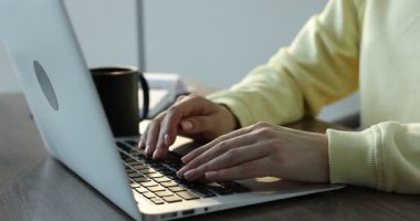 Kapalı alandaki ahşap masada dizüstü bilgisayar kullanan metin yazarı