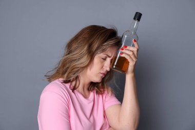 Alkollü içki şişesi olan kadın gri arka planda akşamdan kalma.