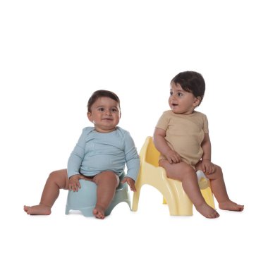 Beyaz arka planda lazımlıkların üzerinde oturan sevimli küçük bebekler.