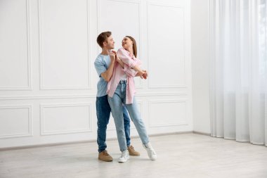 Mutlu çift evde beyaz duvarın yanında dans ediyor.