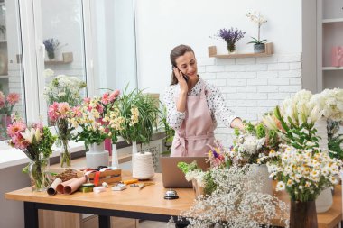 Profesyonel çiçekçi dükkanda çalışırken akıllı telefondan konuşuyor.