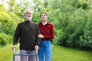 Gülümseyen bakıcı dışarıda yürüyen çerçeveyi kullanan yaşlı bir adamı destekliyor. Metin için boşluk