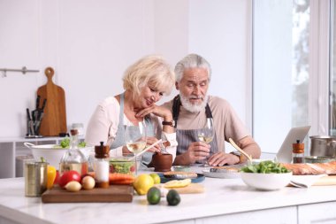 Yaşlı bir çift birlikte yemek pişiriyor ve içeride beyaz şarap içiyor.