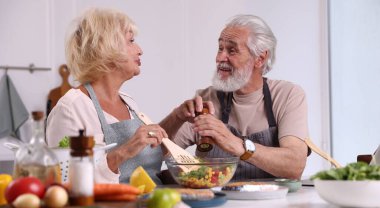 Yaşlı çift içeride birlikte yemek pişiriyor.