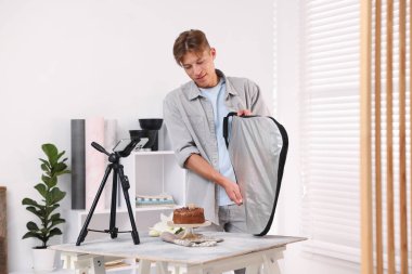 Adam stüdyoda çikolatalı pastanın fotoğrafını çekmek için yansıtıcı kullanıyor. Profesyonel yemek fotoğrafçılığı.