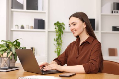 İçerideki ahşap masada dizüstü bilgisayar kullanan metin yazarı