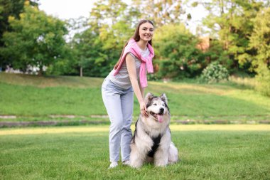 Yeşil çimlerin üzerinde sevimli Alaska köpeğiyle gülümseyen kadın.