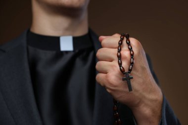 Kahverengi arka planda tespihi olan rahip, yakın plan.