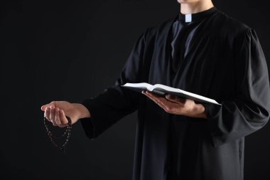 Kutsal İncil 'i olan ve siyah arka planda vaaz veren bir rahip, yakın plan.