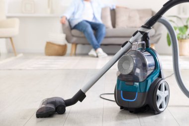 Evdeki kanepede dinlenen adam, elektrik süpürgesine odaklan.