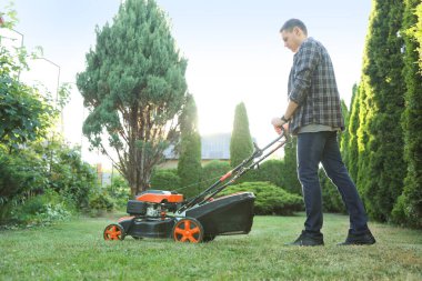 Bahçede çim biçme makinesiyle yeşil çim biçen bir adam