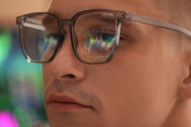 Arka planda yansıması olan gözlük takan genç adam, yakın plan.