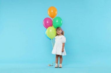 Açık mavi arka planda bir sürü renkli balonu olan şirin bir kız.