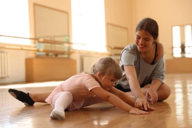 Gülümseyen bale öğretmeni dans dersinde küçük kızın esnemesine yardım ediyor.