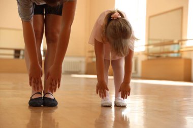 Dans sınıfında küçük bir kızla esneme hareketleri yapan bale öğretmeni.