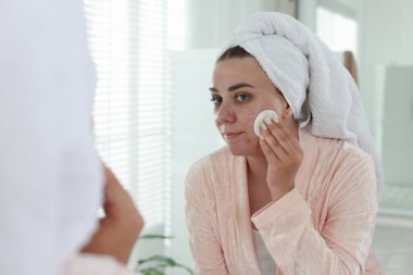 Sivilceli bir kadın aynanın içinde yüzünü temizliyor.