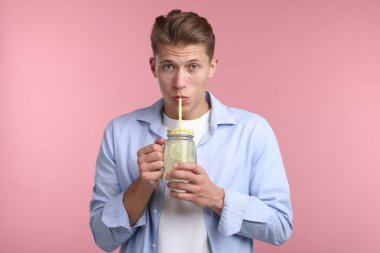 Mason kavanozundan pembe arka planda limonata içen adam. Tazeleyici içecek.