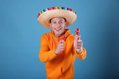 Şapkalı mutlu adam açık mavi arka planda marakas çalıyor.