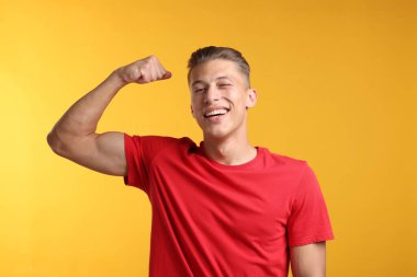 Kuvvet. Sarı arka planda kaslarını gösteren mutlu bir adam.