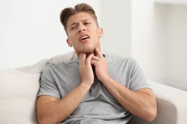 Evdeki kanepede boğaz ağrısı çeken genç bir adam.