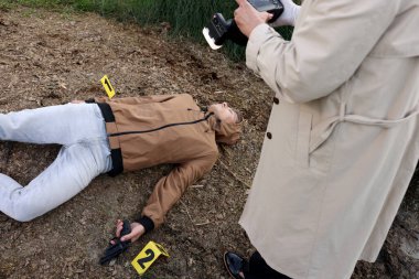 Adli tıp uzmanlığı. Cinayet mahallinde çalışan kameralı bir dedektif. Cesetle birlikte dışarıda, manzaranın üstünde.