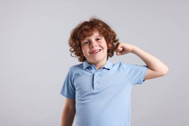 Kuvvet. Küçük mutlu çocuk açık gri arka planda pazılarını gösteriyor.