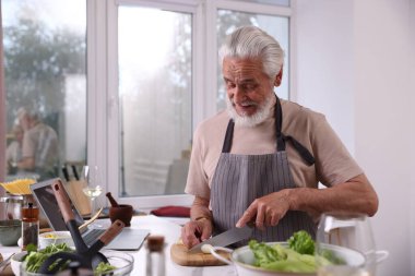 Pencerenin yanındaki masada yaşlı bir adam yemek pişiriyor.