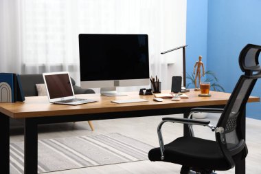 Modern bilgisayarı, diğer cihazları ve ahşap masa üzerindeki kırtasiyesi olan şık bir iş yeri.