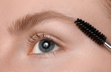 Genç bir kadın kaşlarını hortlakla fırçalıyor, yakın plan.