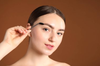 Genç bir kadın kahverengi arka planda kaşlarını korkunç bir şekilde fırçalıyor.