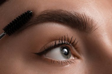 Genç bir kadın kaşlarını hortlakla fırçalıyor, yakın plan.