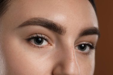 Kahverengi arka planda güzel kaşları olan genç bir kadın, yakın plan.