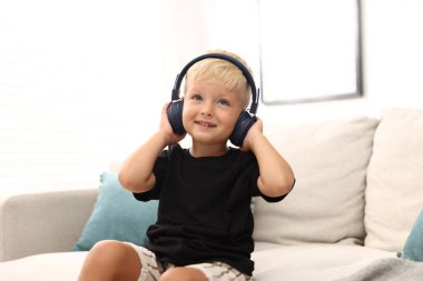 Evdeki kanepede kulaklıklı şirin bir çocuk.