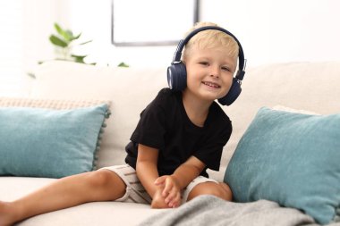 Evdeki kanepede kulaklıklı şirin bir çocuk.