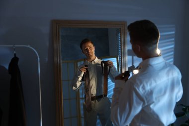 Kapalı alanda aynanın yanında kravat seçen bir adam.