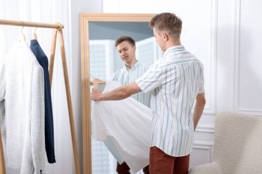 Hazırlanıyor. Genç adam aynanın yanında kıyafet deniyor.