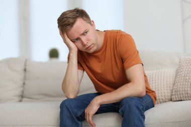 Evdeki kanepede üzgün, düşünceli bir adam.