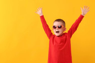 Güneş gözlüklü şirin çocuk sarı arka planda gülüyor.