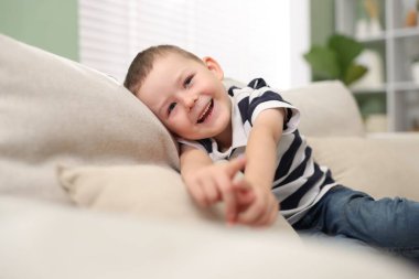 Şirin küçük çocuk kanepede bir şeyi gösterip gülüyor.