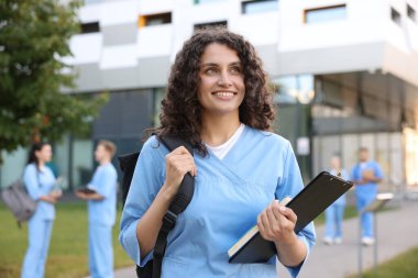 Sırt çantası, not defteri ve not defteri açık havada seçici bir odak noktası olan üniformalı bir tıp öğrencisi.