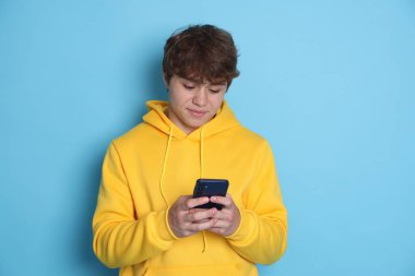 Genç çocuk açık mavi arka planda akıllı telefon kullanıyor.
