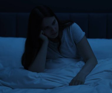 Evdeki yatakta oturan üzgün genç kadın.