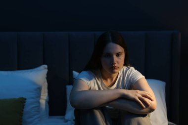 Evdeki yatakta oturan üzgün genç kadın.